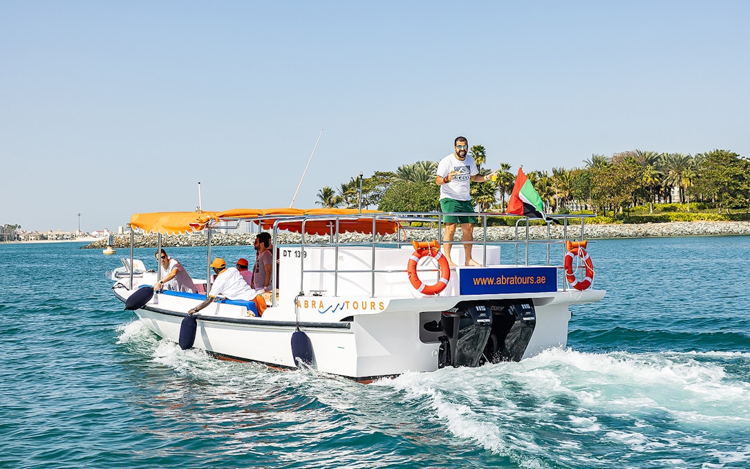 Private small group on a boat cruise in Dubai with UAE flag and coastal view.
