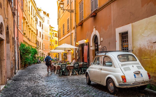 Cobblestone street in Rome with outdoor café and vintage car, near Carcer Tullianum.