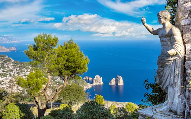 Capri coastline view with Faraglioni rocks and statue, seen from a hillside vantage point.