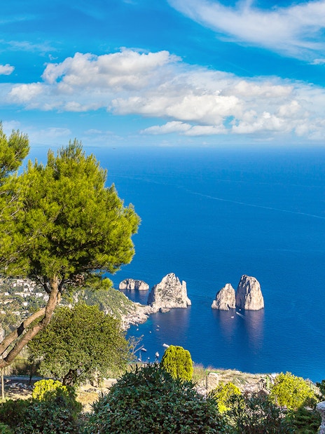 Capri coastline view with Faraglioni rocks and statue, seen from a hillside vantage point.