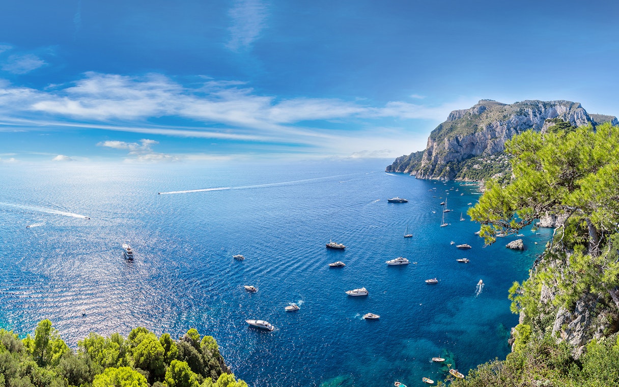 Boats in the blue waters near Capri with cliffs and greenery, view from Pompeii.
