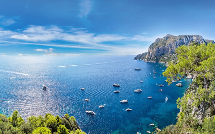 Boats in the blue waters near Capri with cliffs and greenery, view from Pompeii.