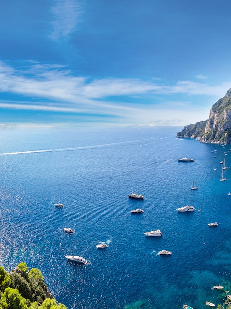 Boats in the blue waters near Capri with cliffs and greenery, view from Pompeii.