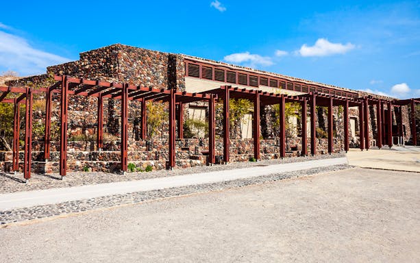 Akrotiri archaeological site entrance with stone walls and wooden beams.