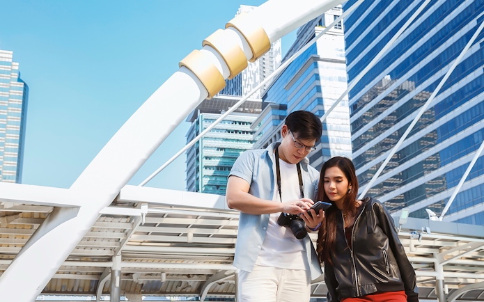 Couple using smartphone in Singapore city with modern architecture in background.