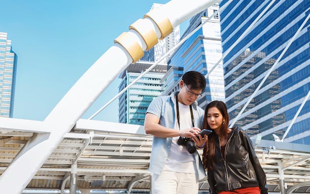 Couple using smartphone in Singapore city with modern architecture in background.