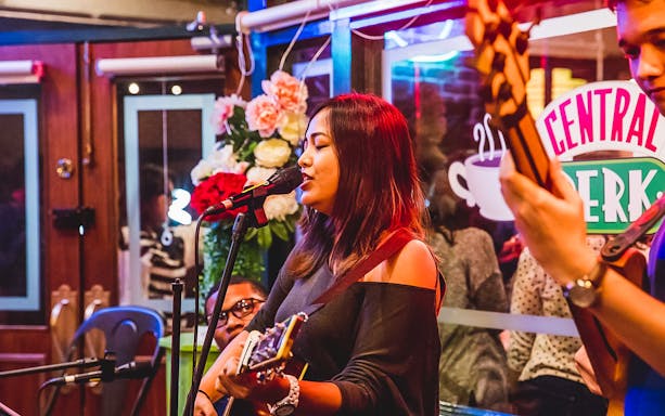 Musician performing at Central Perk Singapore with guitar and microphone.