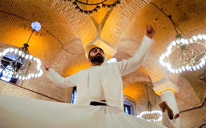Whirling Dervish performing in traditional attire under ornate chandeliers in Istanbul.