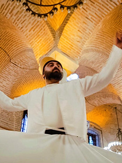 Whirling Dervish performing in traditional attire under ornate chandeliers in Istanbul.