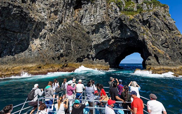 Tourists on a boat approaching the Hole in the Rock at Bay of Islands, New Zealand.