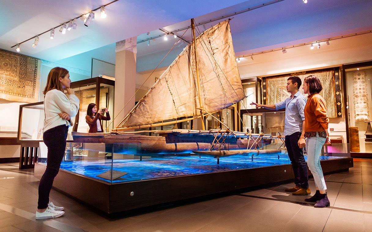 Visitors observing a traditional boat exhibit at Auckland War Memorial Museum.