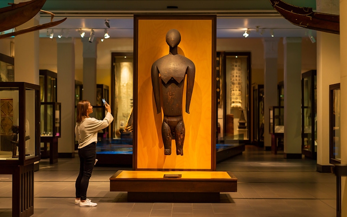Visitor photographing a wooden sculpture at Auckland War Memorial Museum.