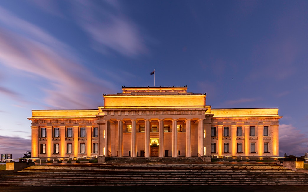 Auckland War Memorial Museum illuminated at dusk with grand columns and steps.