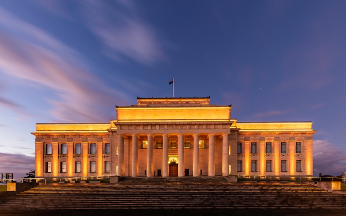 Auckland War Memorial Museum illuminated at dusk with grand columns and steps.