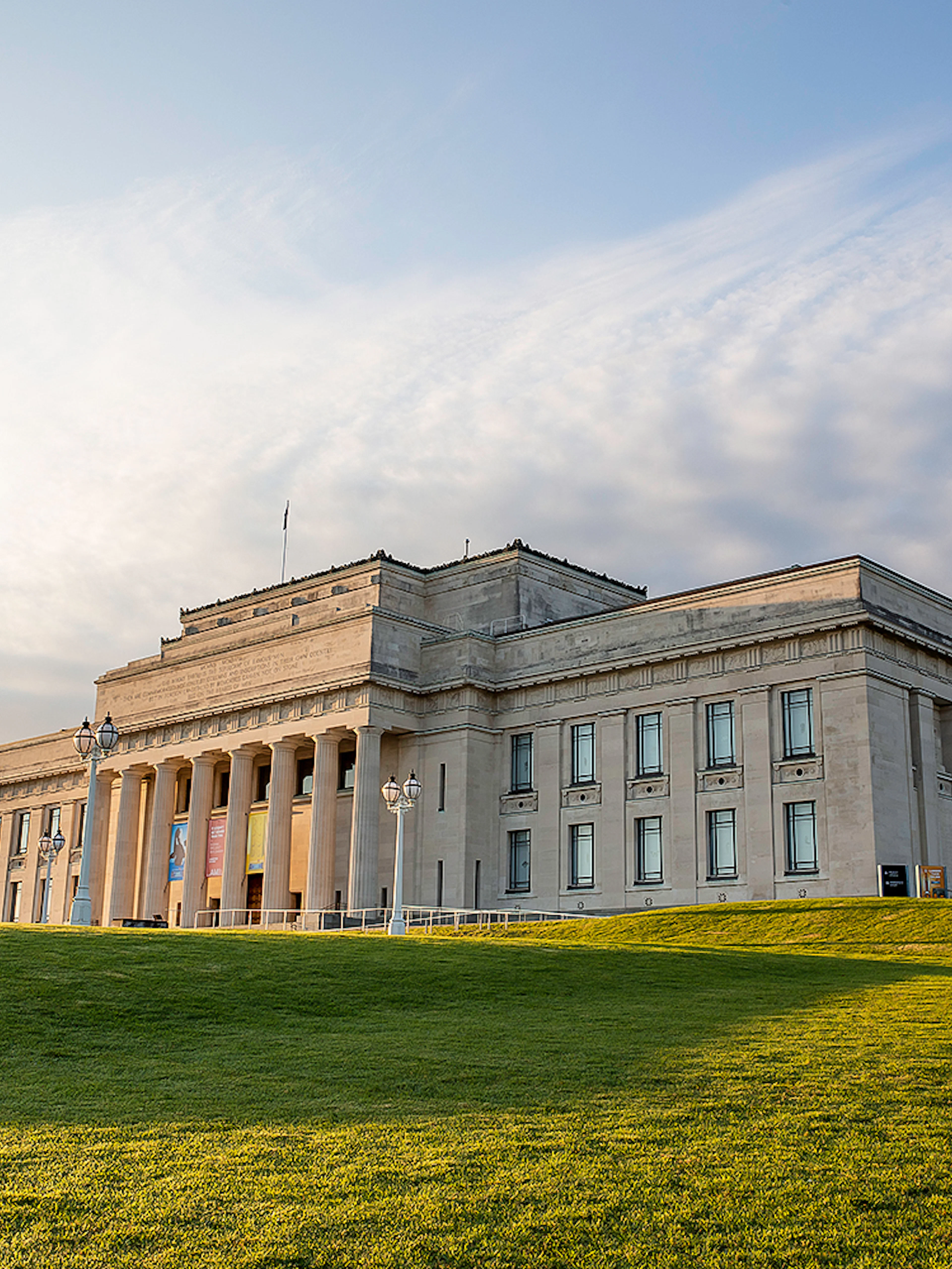 Auckland War Memorial Museum with surrounding green lawn under a cloudy sky.
