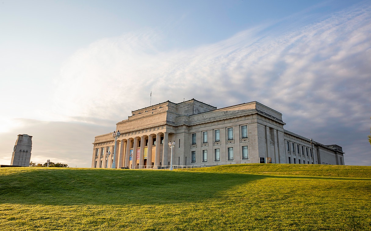 Auckland War Memorial Museum with surrounding green lawn under a cloudy sky.