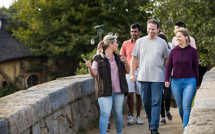 Group walking tour at Hobbiton Movie Set, New Zealand, with guide explaining site features.