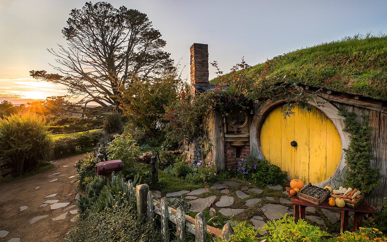 Hobbiton Movie Set with round yellow door and garden path at sunset, Rotorua tour.