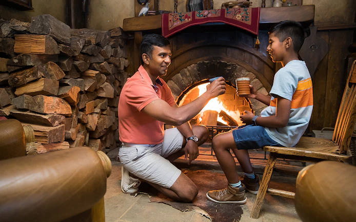 Father and son enjoying drinks by the fireplace at Hobbiton Movie Set, Rotorua tour.