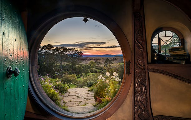 View from Hobbiton Movie Set door at sunset, featuring gardens and distant hills.