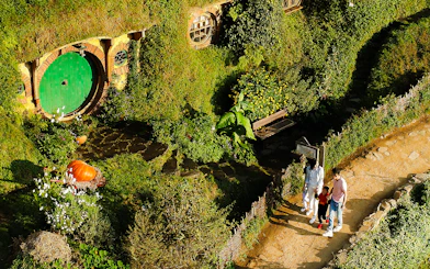 Hobbiton Movie Set tour with visitors near a hobbit hole in lush greenery, Rotorua.