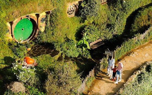 Hobbiton Movie Set tour with visitors near a hobbit hole in lush greenery, Rotorua.