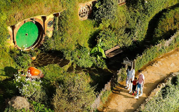 Hobbiton Movie Set tour with visitors near a hobbit hole in lush greenery, Rotorua.