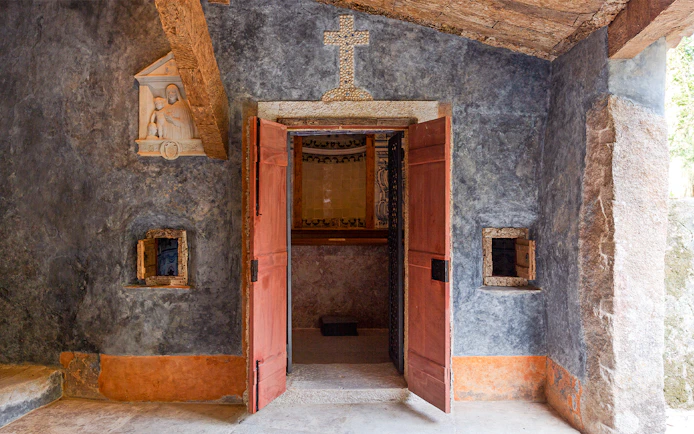 Convento dos Capuchos entrance with open wooden doors and stone cross above, Sintra, Portugal.