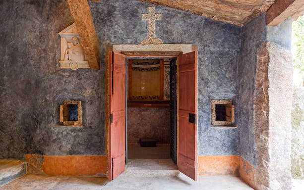 Convento dos Capuchos entrance with open wooden doors and stone cross above, Sintra, Portugal.
