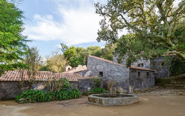 Convento dos Capuchos courtyard with stone buildings and lush greenery in Sintra, Portugal.