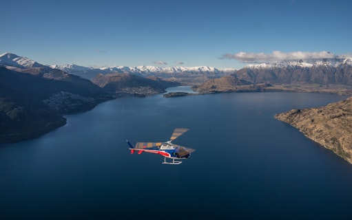 Helicopter flying over Lake Wakatipu with snow-capped mountains in Queenstown, New Zealand.