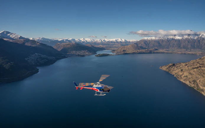 Helicopter flying over Lake Wakatipu with snow-capped mountains in Queenstown, New Zealand.