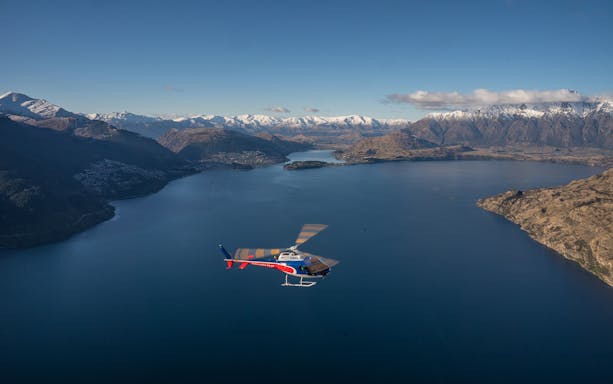 Helicopter flying over Lake Wakatipu with snow-capped mountains in Queenstown, New Zealand.