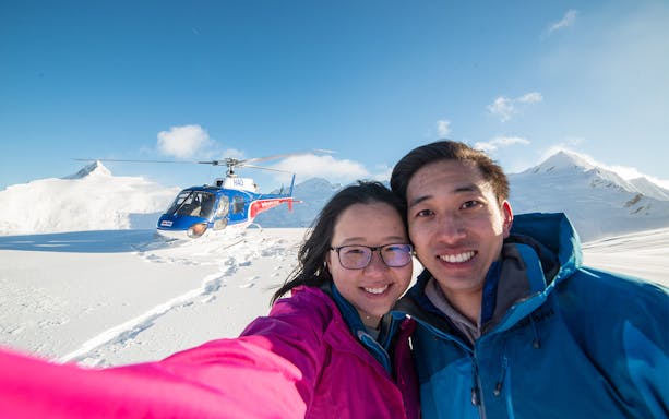 Couple on snow-covered mountain with helicopter during Queenstown Panorama Helicopter Tour.