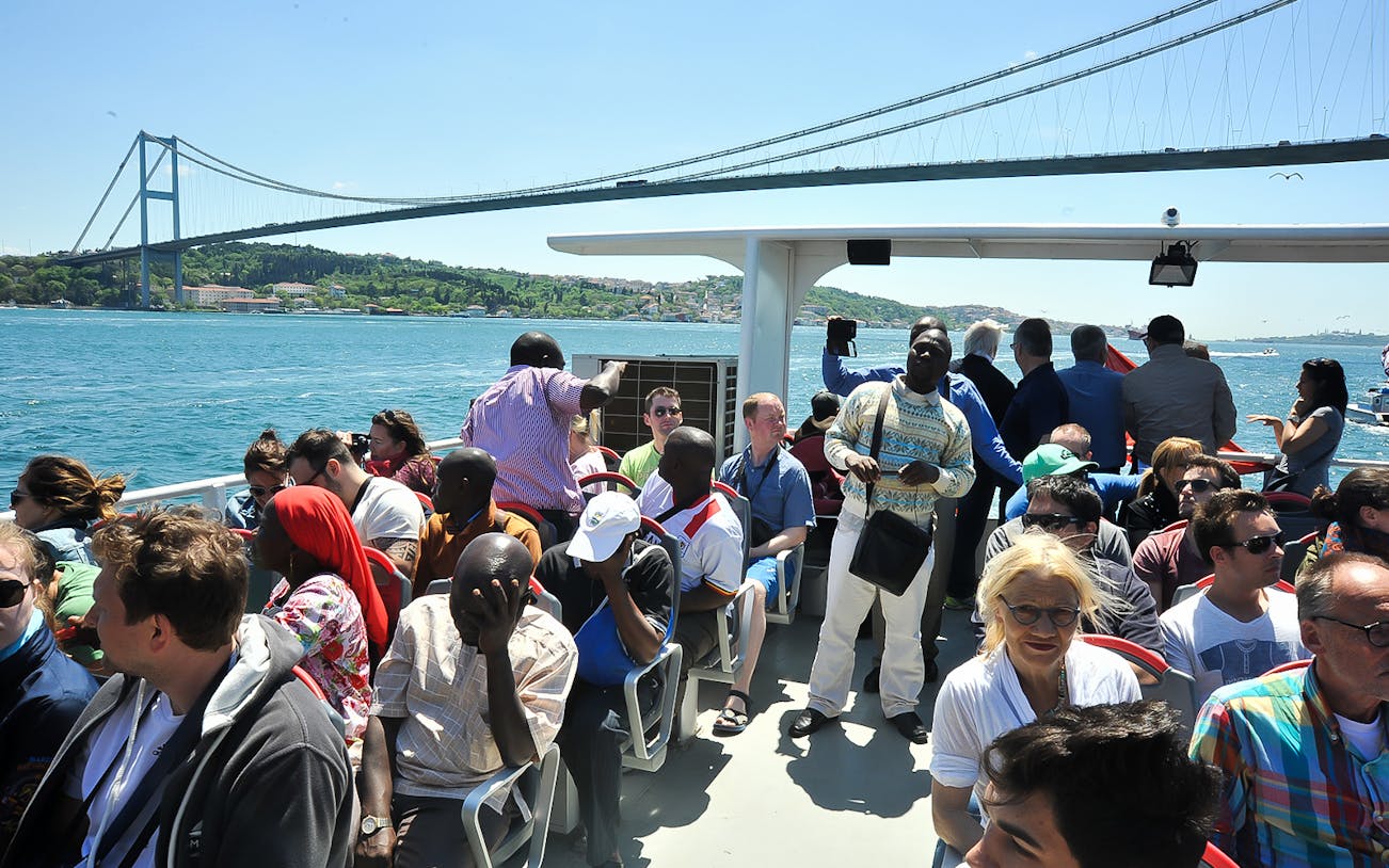 Tourists enjoying a Bosphorus cruise with a view of the Bosphorus Bridge in Istanbul.