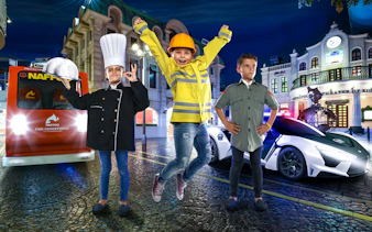 Children in firefighter, chef, and pilot costumes at KidZania Dubai with fire truck and police car.