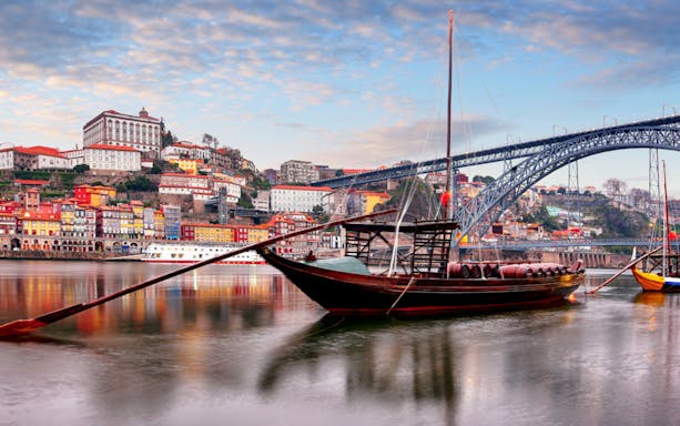 Traditional boat on Douro River with Porto cityscape and Dom Luís I Bridge.