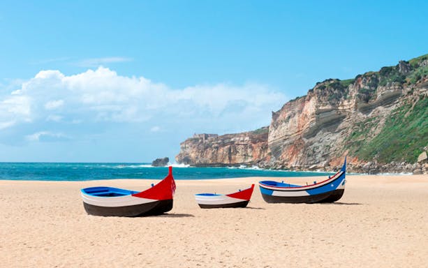 Traditional fishing boats on Nazaré beach with cliffs in the background, Portugal.