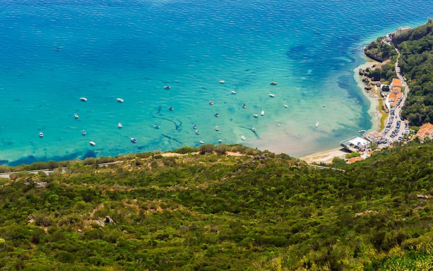 Aerial view of Arrábida coastline with boats in turquoise water, part of a wine tour from Lisbon.