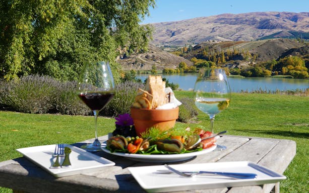 Wine glasses and platter on a table overlooking a lake and hills in Queenstown.