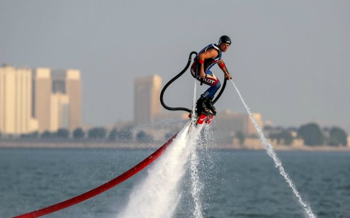Person jetpacking over water with city skyline in the background.