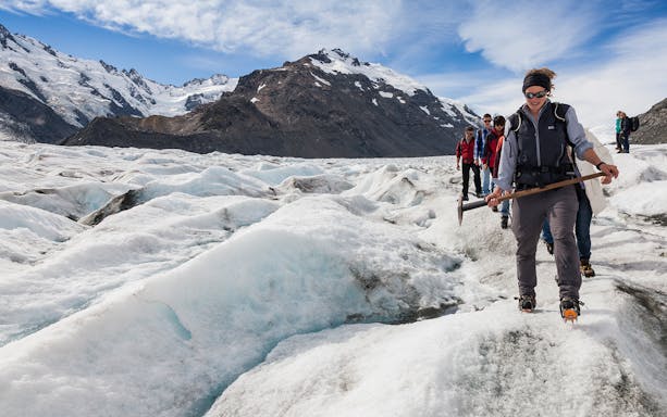 Group hiking on Tasman Glacier with ice axes and crampons.