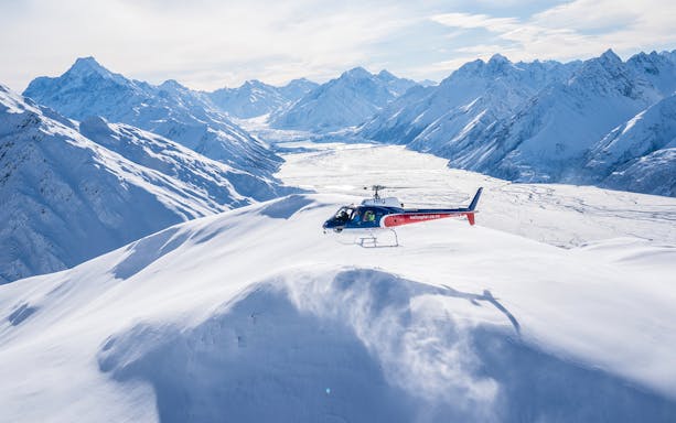 Helicopter flying over snow-covered Mount Cook with alpine landing site.