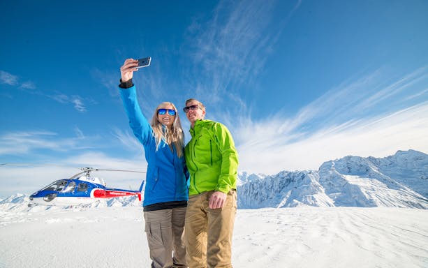 Couple taking selfie during helicopter tour with alpine landing on Mount Cook.