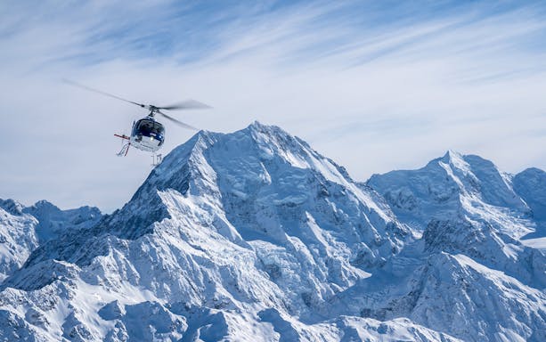 Helicopter flying over snow-covered Mount Cook with alpine landing site.