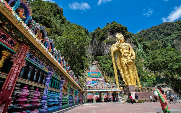 Batu Caves entrance with colorful steps and large golden statue, Kuala Lumpur.