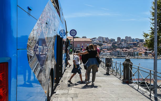 Hop-on hop-off tour bus in Porto with passengers boarding by the riverside.