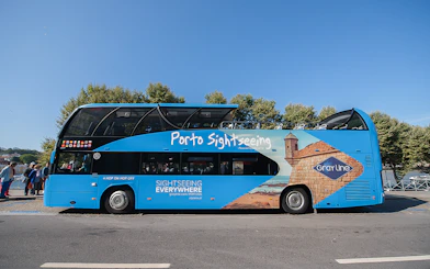 Porto sightseeing bus for hop-on hop-off tour with cityscape in background.