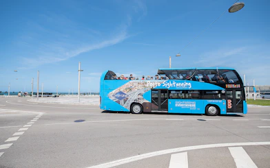 Open-top blue sightseeing bus on Porto hop-on hop-off tour near the coast.