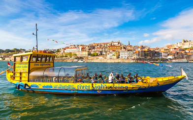 Sightseeing boat on Douro River with Porto cityscape in the background.